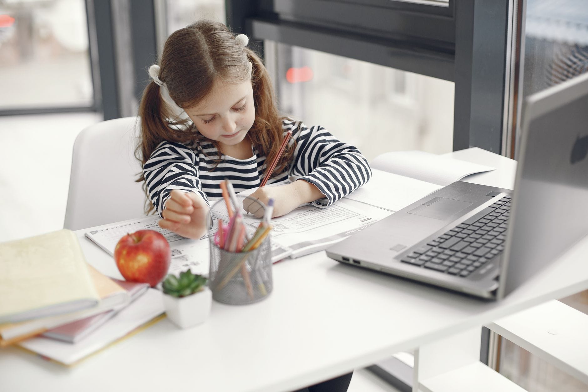Dziewczynka uczy się w domu przy laptopie i zeszytach