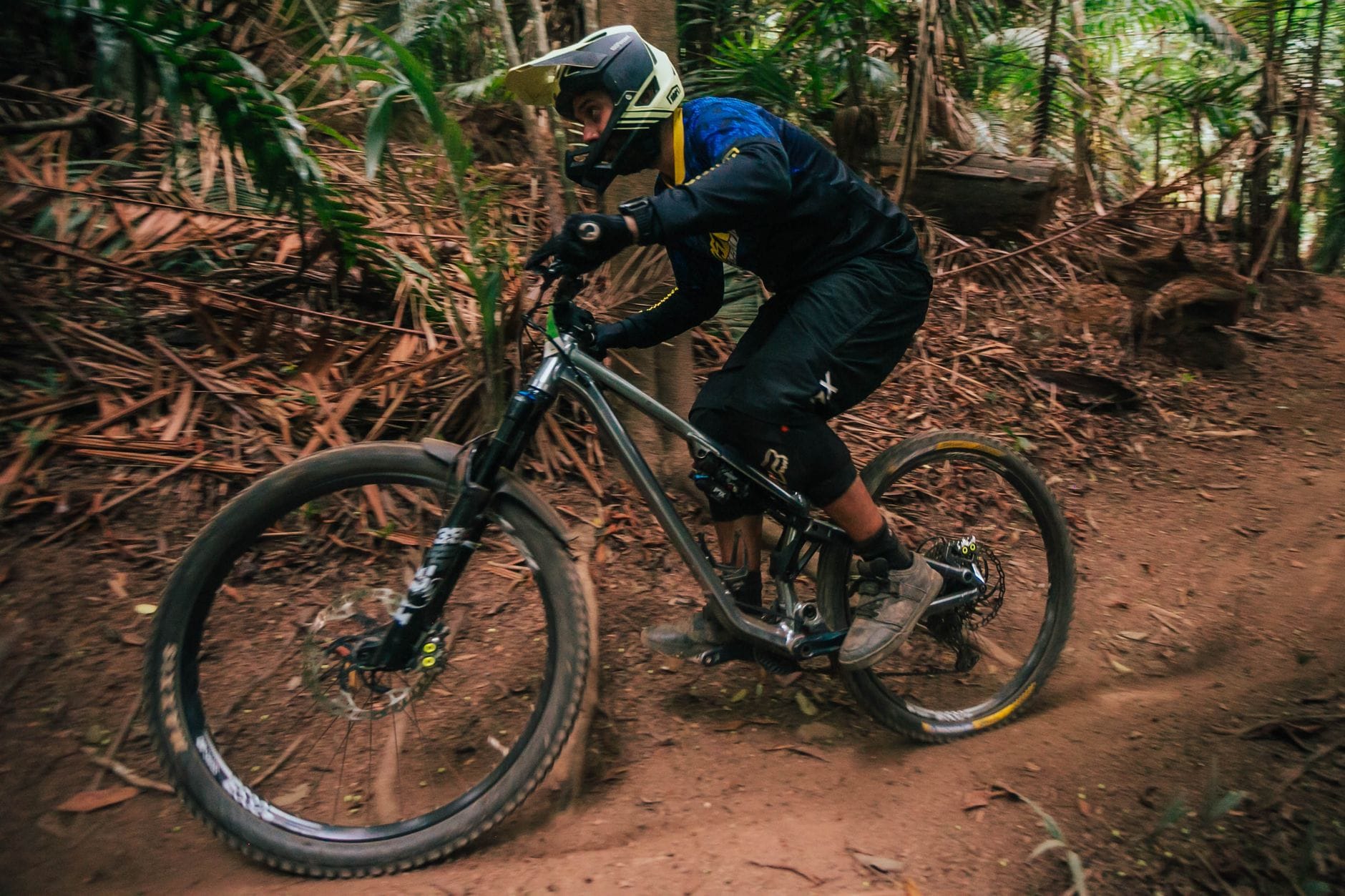 Enduro rider w pełnym kasku jedzie agresywnie leśnym singletrackiem