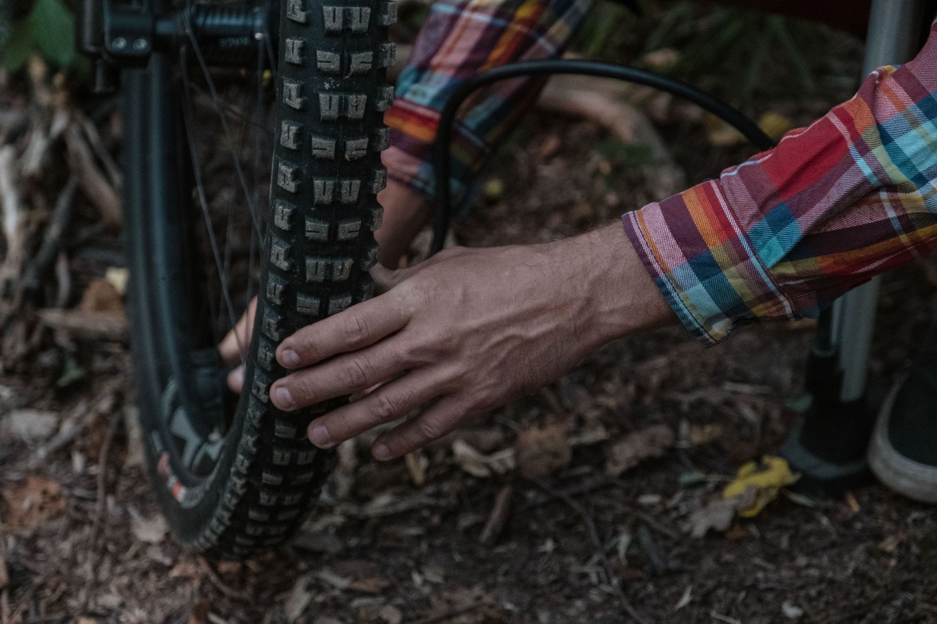 Serwisant w koszuli w kratę pompuje oponę roweru enduro w terenie