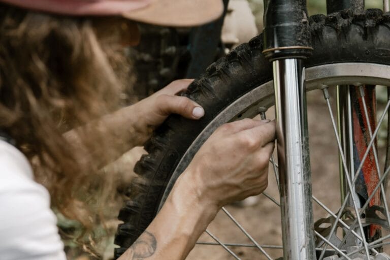 Zbliżenie na dłonie mechanika naprawiającego oponę roweru terenowego na zewnątrz
